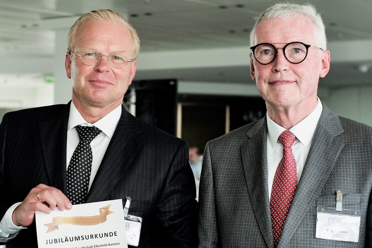 Zwei Männer blicken in die Kamera. Einer hält ein Blatt mit der Aufschrift Jubiläumsurkunde in die Kamera.